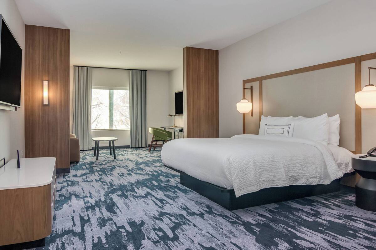 Habitación de hotel con una cama grande, un escritorio, una silla, un televisor y una ventana con cortinas.