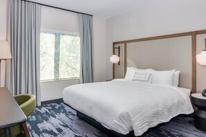 Ein Hotelzimmer mit einem großen Bett, einem Schreibtisch, einem Stuhl und einem Fenster mit Vorhängen.