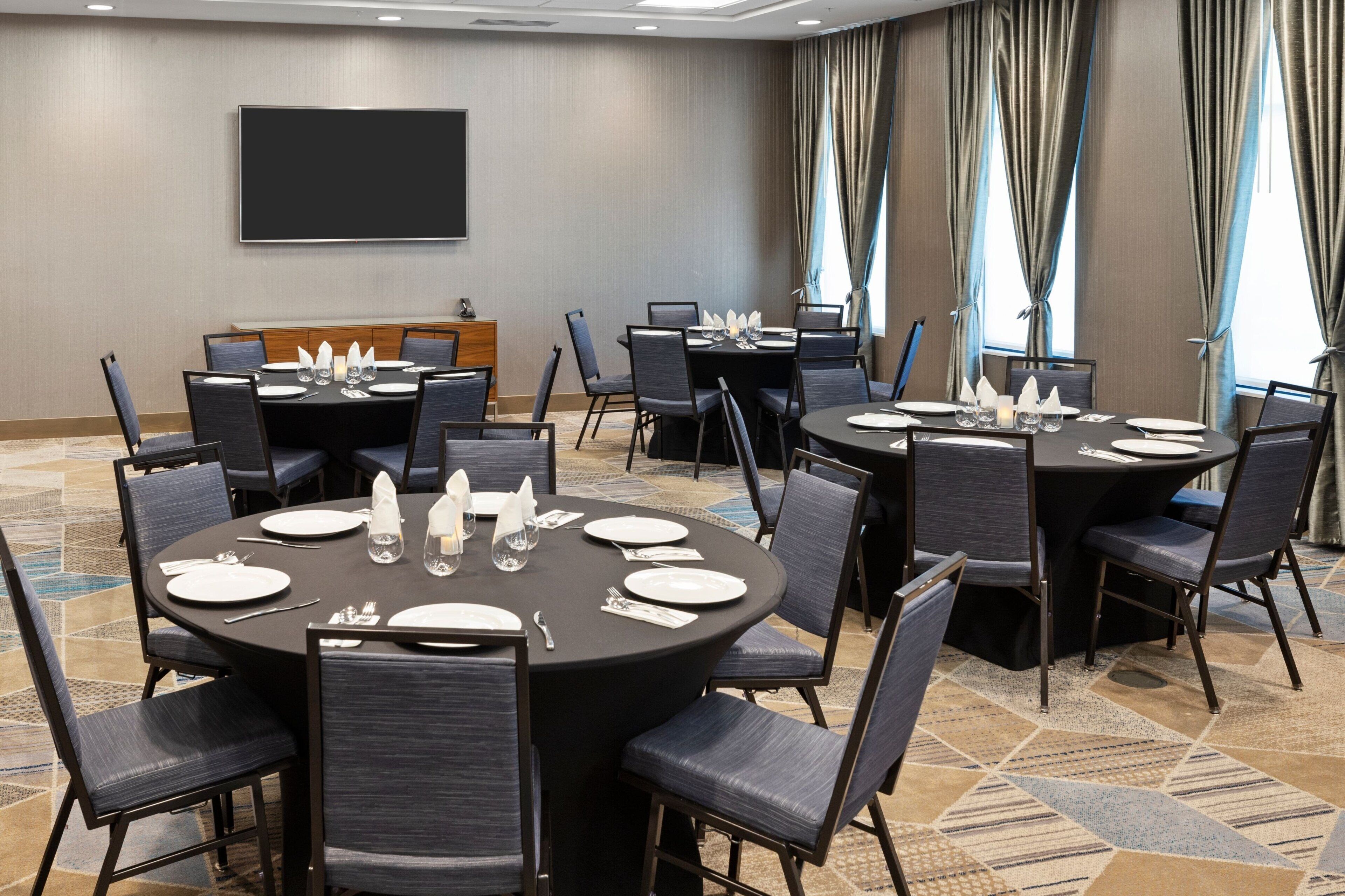 Un salón de conferencias con varias mesas redondas, cada una dispuesta con platos, cubiertos y vasos.