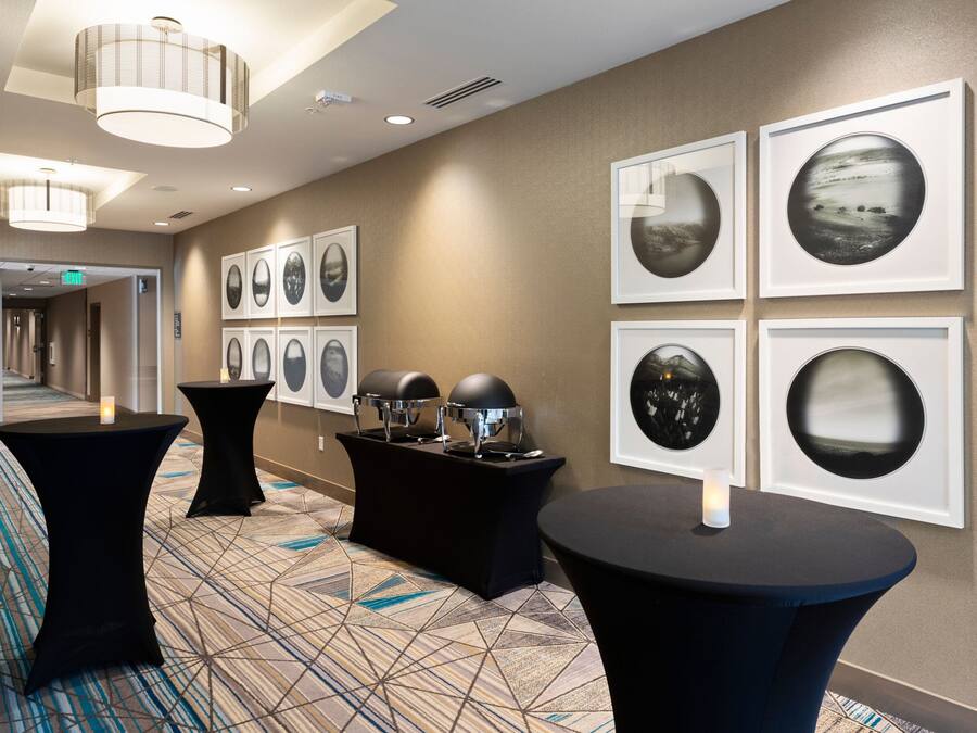 A hotel lobby with a geometric patterned carpet, black round tables with candles, and framed artwork on the walls.