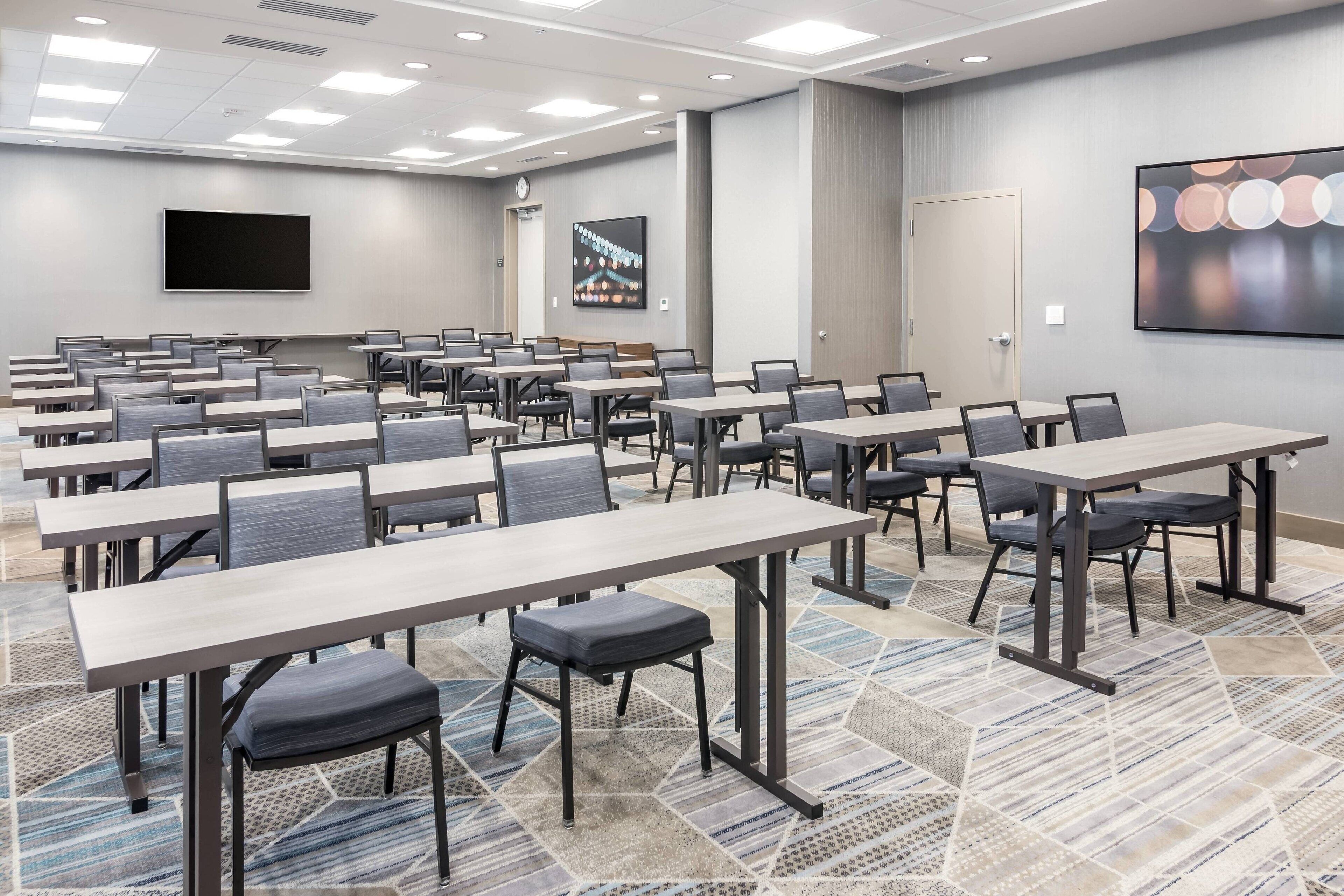 A conference room with multiple tables and chairs, a large screen, and artwork on the walls.