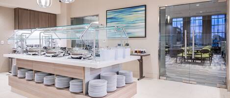 Un buffet avec plusieurs points de service, une cloison en verre et des assiettes soigneusement empilées.