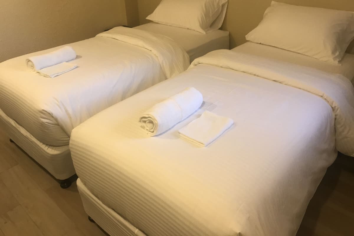 Two single beds with white linens and towels, a wooden floor, and beige walls.
