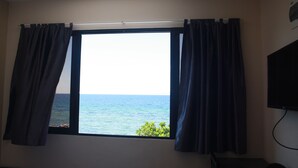 Ein Zimmer mit großem Fenster, Vorhängen, einem Flachbildfernseher und einem kleinen Tisch.
