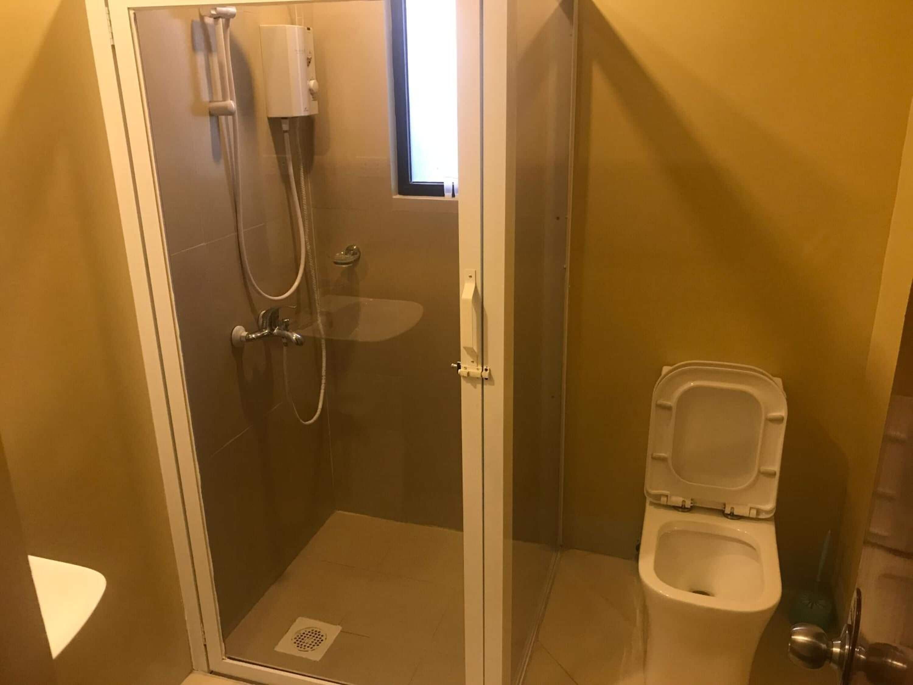 A small, enclosed shower area with a glass door, a toilet, and a window.