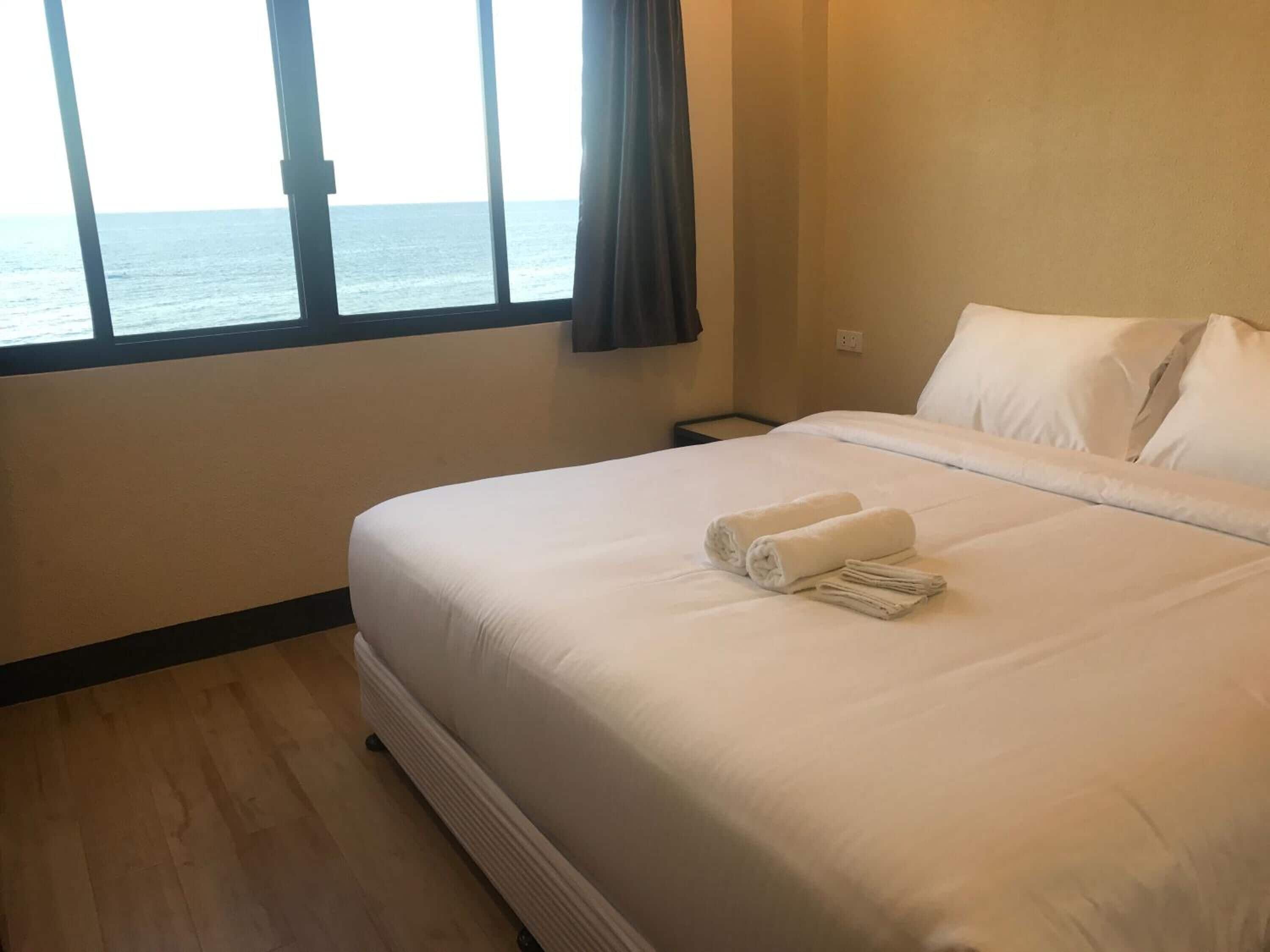 A hotel room with a large bed, a nightstand, and a view of the sea through a window.