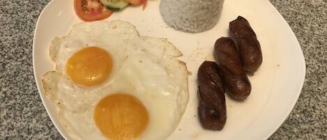 A plate with fried eggs, sausages, rice, and sliced tomatoes and cucumbers.