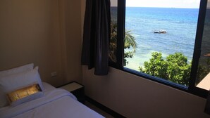 Ein Hotelzimmer mit Bett, einem Fenster mit Blick auf das Meer und ein Boot, sowie einem Vorhang.
