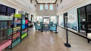 A spacious lobby with a herringbone floor, a chandelier, and a reception desk with teal chairs.