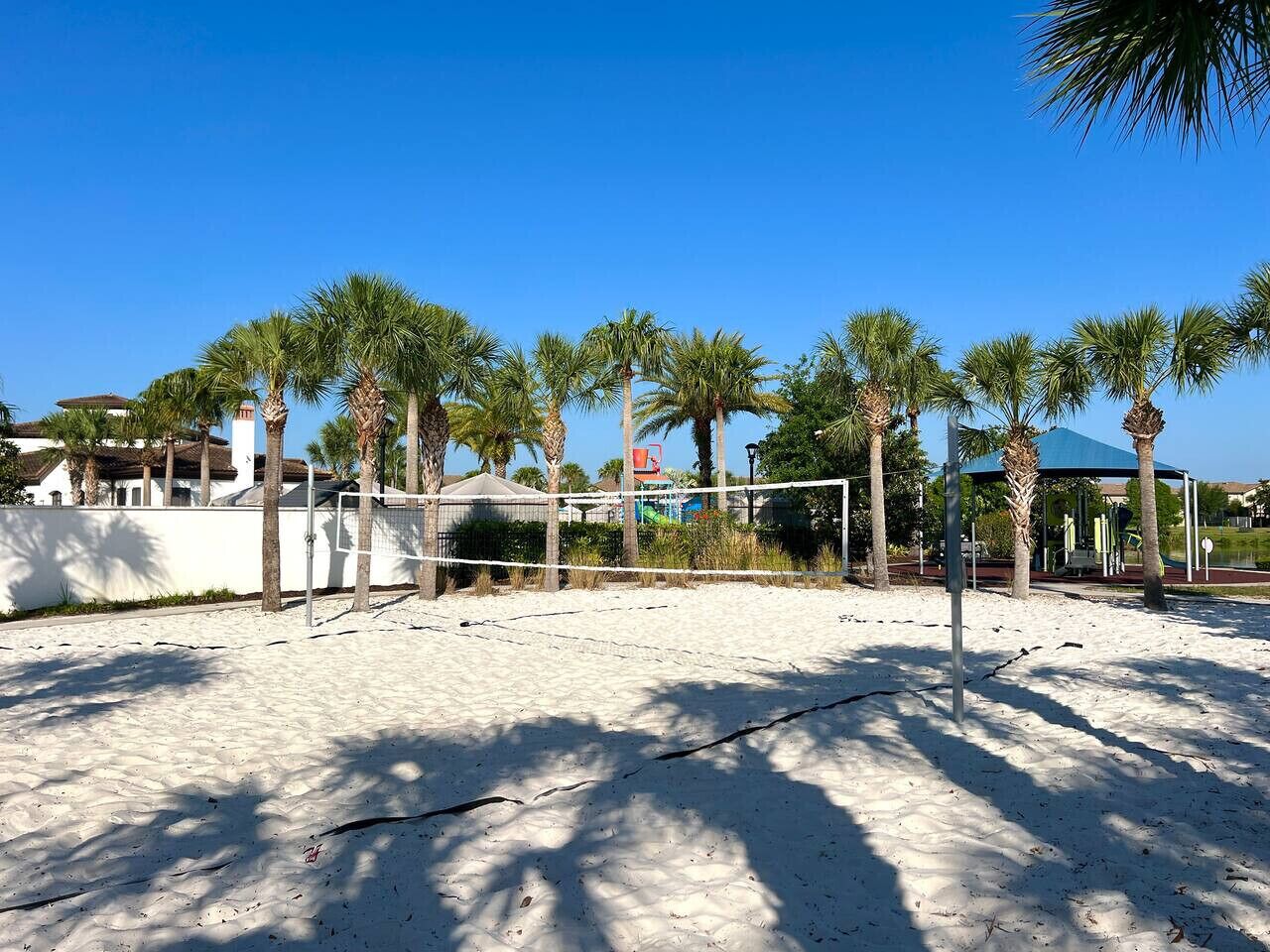 Een strandvolleybalveld met palmbomen, een overdekt zitgedeelte en een helderblauwe lucht.