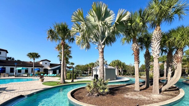 A pool area with palm trees, a small island, and a building in the background.