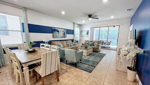 A spacious living room with a dining area, a ceiling fan, and large windows.