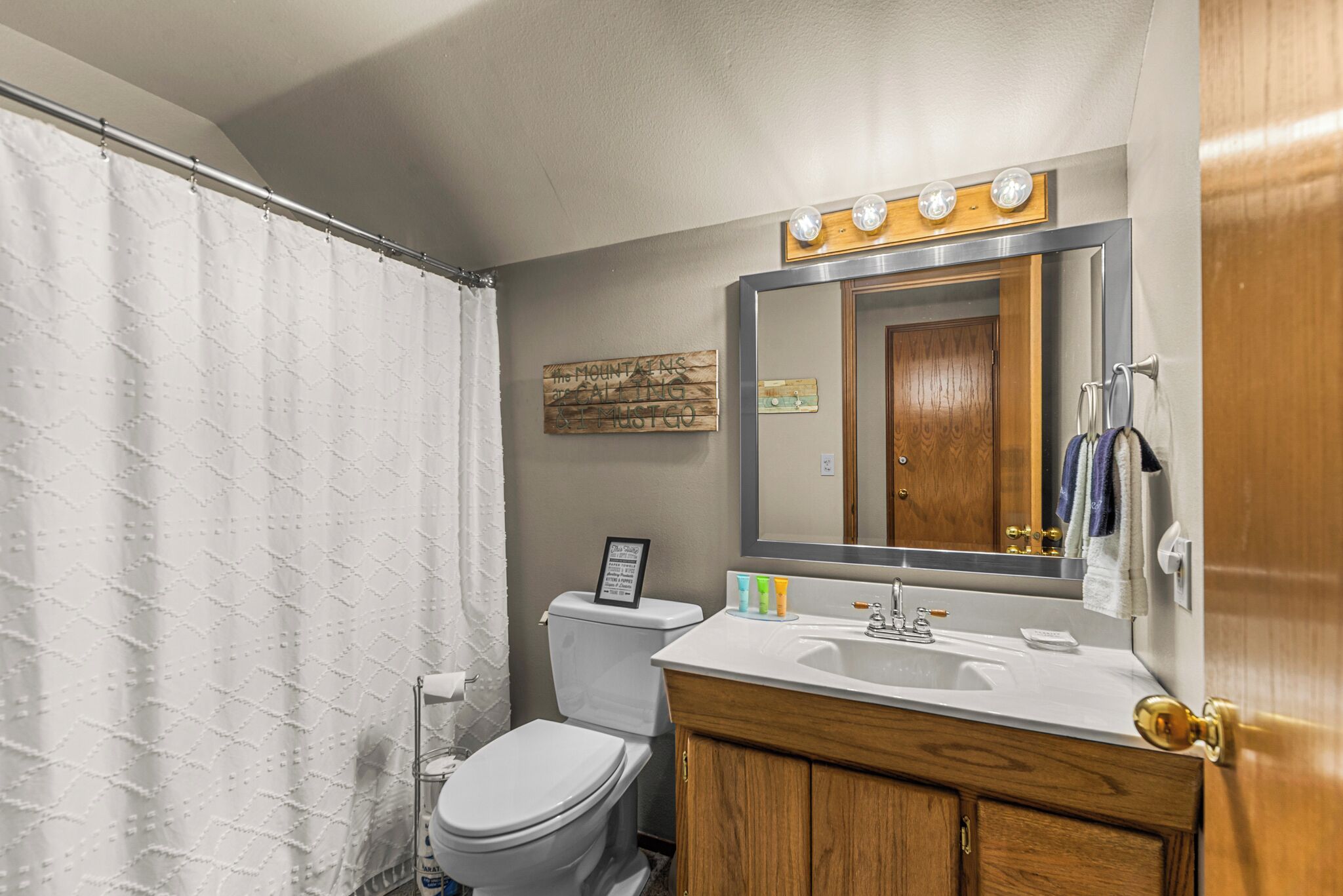A bathroom with a shower curtain, toilet, sink, mirror, and wooden cabinet.