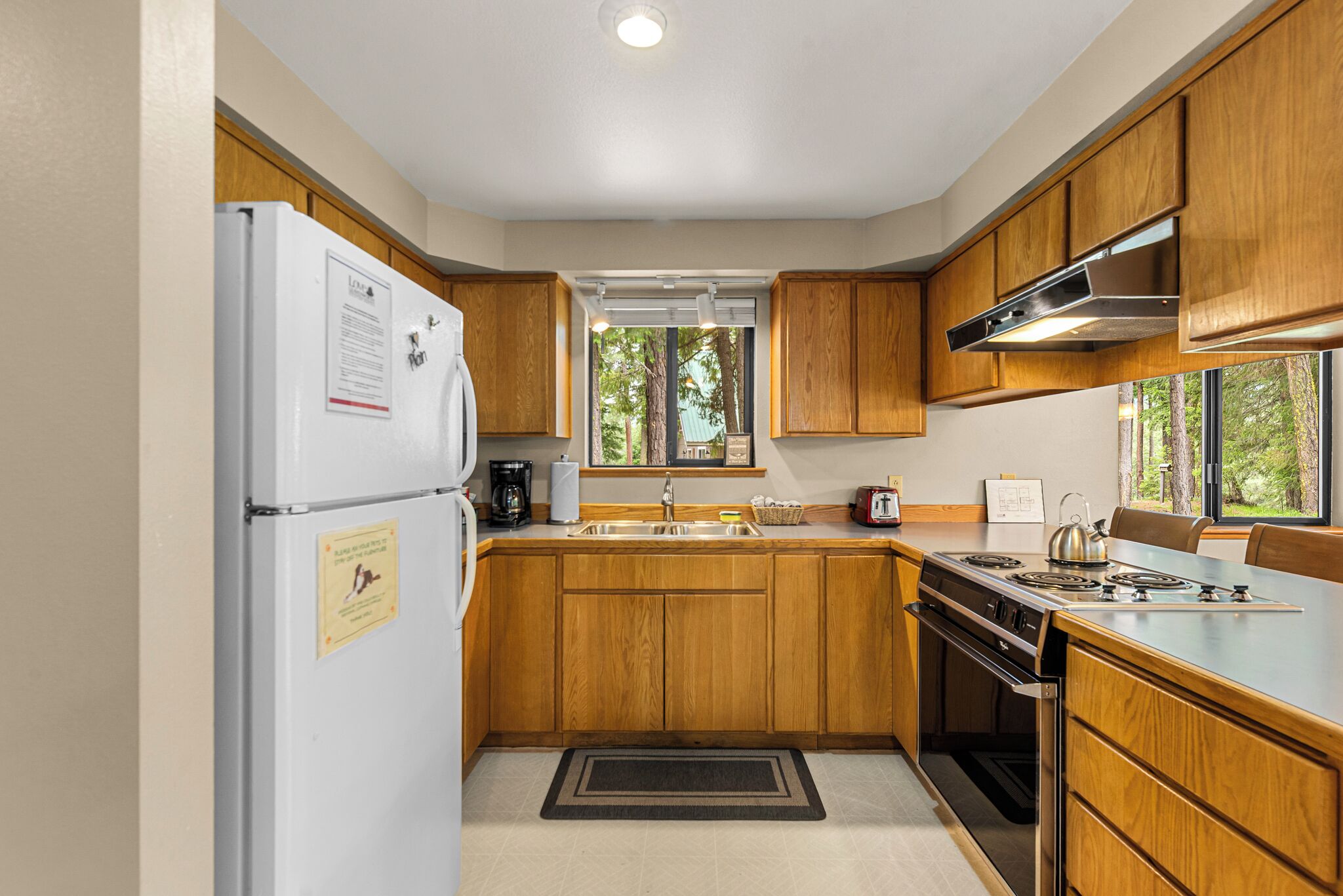 Una cocina con armarios de madera, campana extractora de acero inoxidable, refrigerador y una ventana que proporciona luz natural.