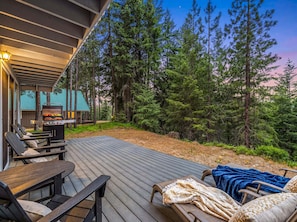 A deck with outdoor furniture, a grill, and a view of a forest.