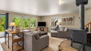 A living room with a fireplace, sofas, a TV, and large windows. - Sugar Shack - Peaceful and Private Remodeled Cabin (Leavenworth)