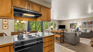 A modern kitchen with wooden cabinets, a built-in stove, and a dining area with a table and chairs. - Sugar Shack - Peaceful and Private Remodeled Cabin (Leavenworth)