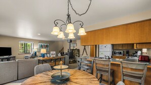 A modern kitchen with wooden cabinets, a dining area with a round table, and a living room with a sofa and TV. - Sugar Shack - Peaceful and Private Remodeled Cabin (Leavenworth)