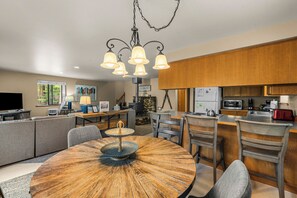 Una cocina moderna con armarios de madera, una zona de comedor con una mesa redonda y una sala de estar con sofá y televisor.