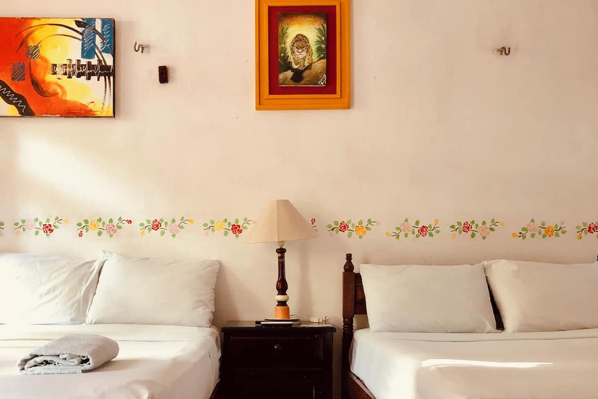 Een hotelkamer met twee enkele bedden, een nachtkastje met een lamp, een lijst met een foto aan de muur en een decoratief vloerkleed.