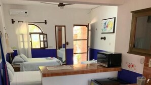 A compact kitchen with a microwave, sink, and refrigerator. There is a dining area with a table set for two, and a small seating area with a sofa and a chair.