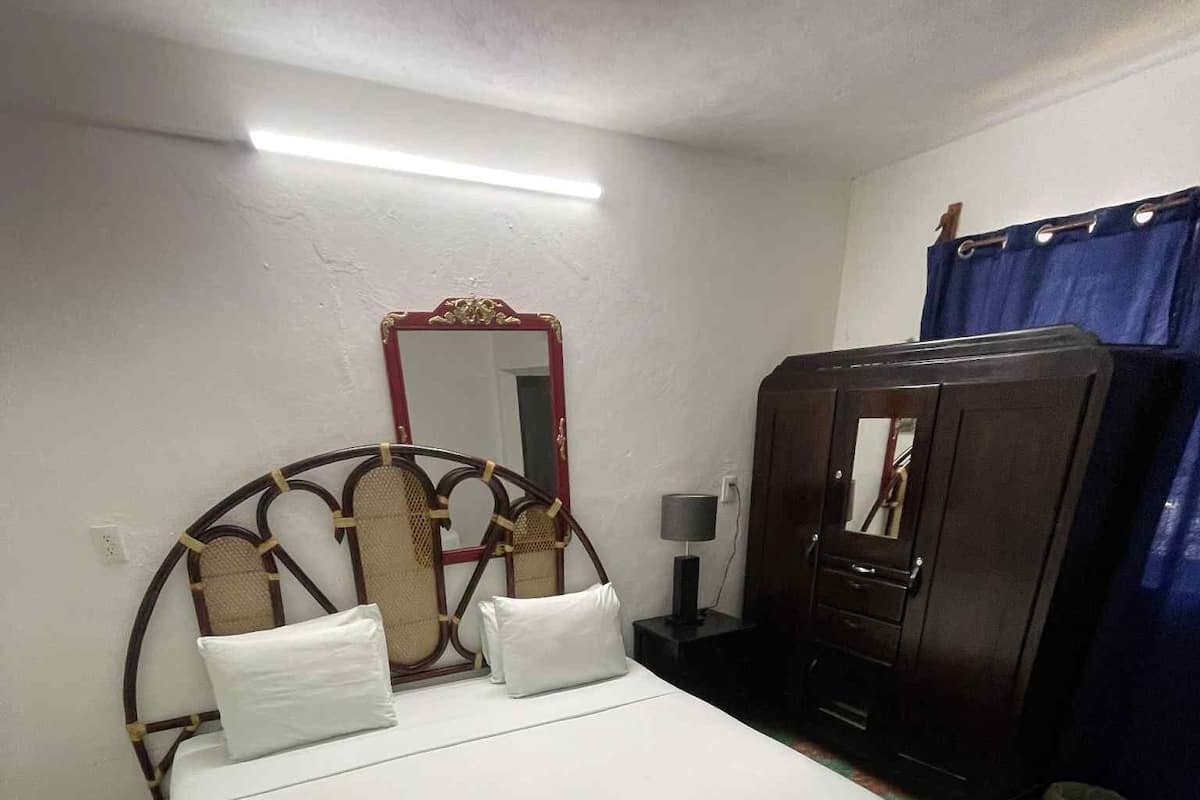 Een kamer met een bed, een dressoir, een spiegel en een kamerkleed met een patroon.