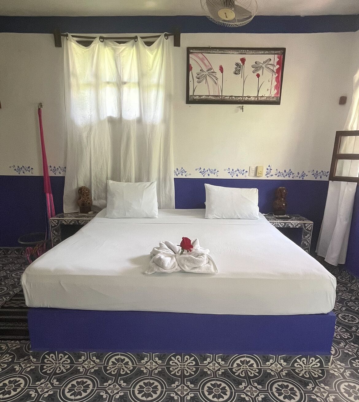 A hotel room with a neatly made bed, a decorative painting, and patterned floor tiles.