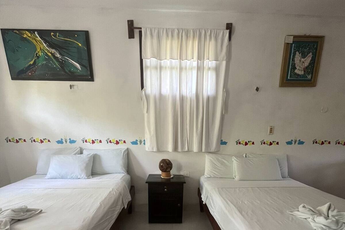 Een kamer met twee eenpersoonsbedden, een klein dressoir, een vloerkleed en een schilderij aan de muur.