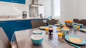 A modern kitchen with blue cabinets, a stainless steel range hood, and a dining area with a table set for breakfast.