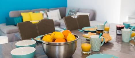 A breakfast setting with a table set for two, featuring a bowl of oranges, a glass of orange juice, and a plate with a folded omelette.