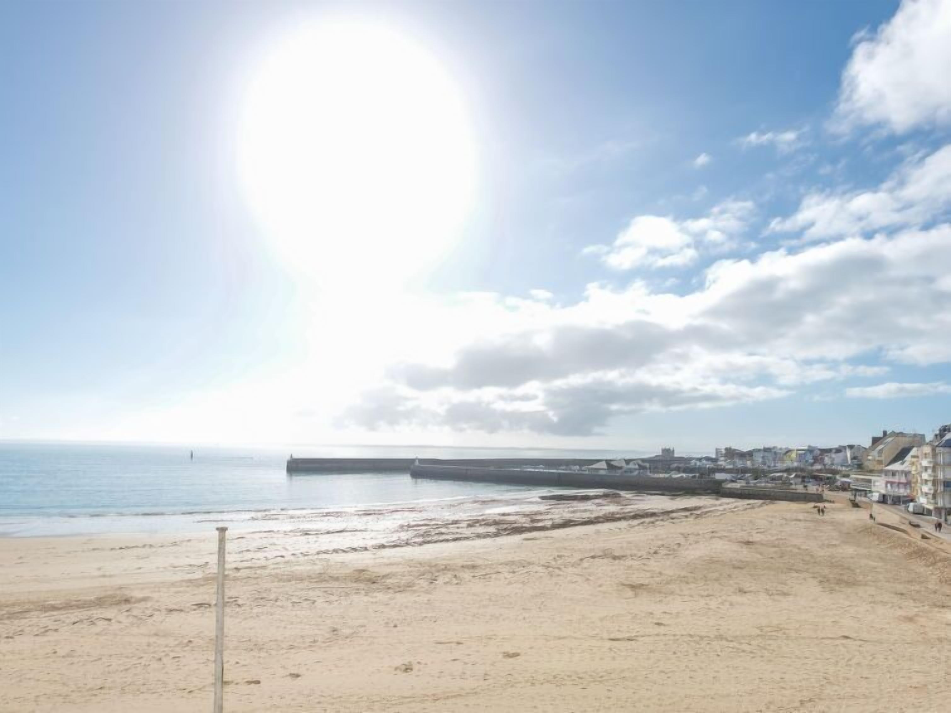 A beach with a pier extending into the water, buildings along the shore, and a clear sky.