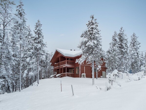 Un gran albergue de madera con balcón, rodeado de árboles cubiertos de nieve.