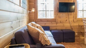 Un interior de cabaña acogedor con una pared de madera, un ventanal grande, un televisor de pantalla plana y un sofá con cojines.