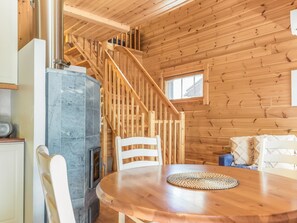 Interior de una cabaña de madera con chimenea de piedra, una mesa redonda de madera y una escalera.