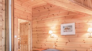 Una habitación de cabaña de madera con una cama, dos lámparas fijadas a la pared y un cuadro enmarcado.