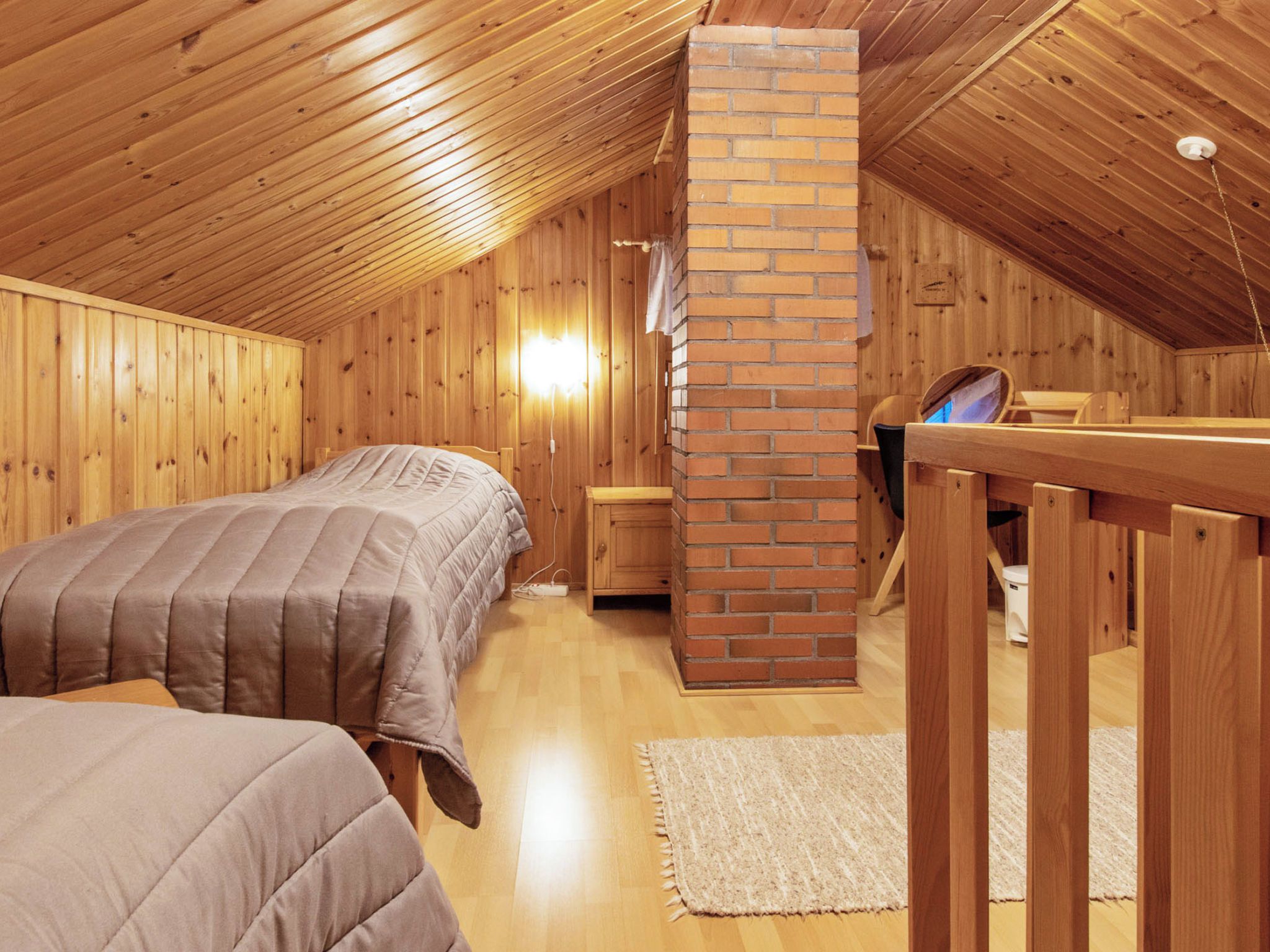 A cozy attic bedroom with wooden walls and a brick chimney. There are two beds with matching bedding and a small wooden table.