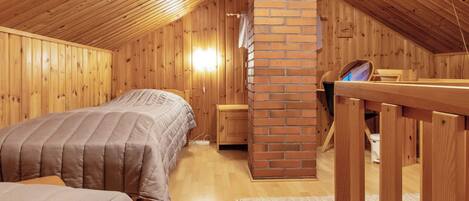A cozy attic bedroom with wooden walls and a brick chimney. There are two beds with matching bedding and a small wooden table.