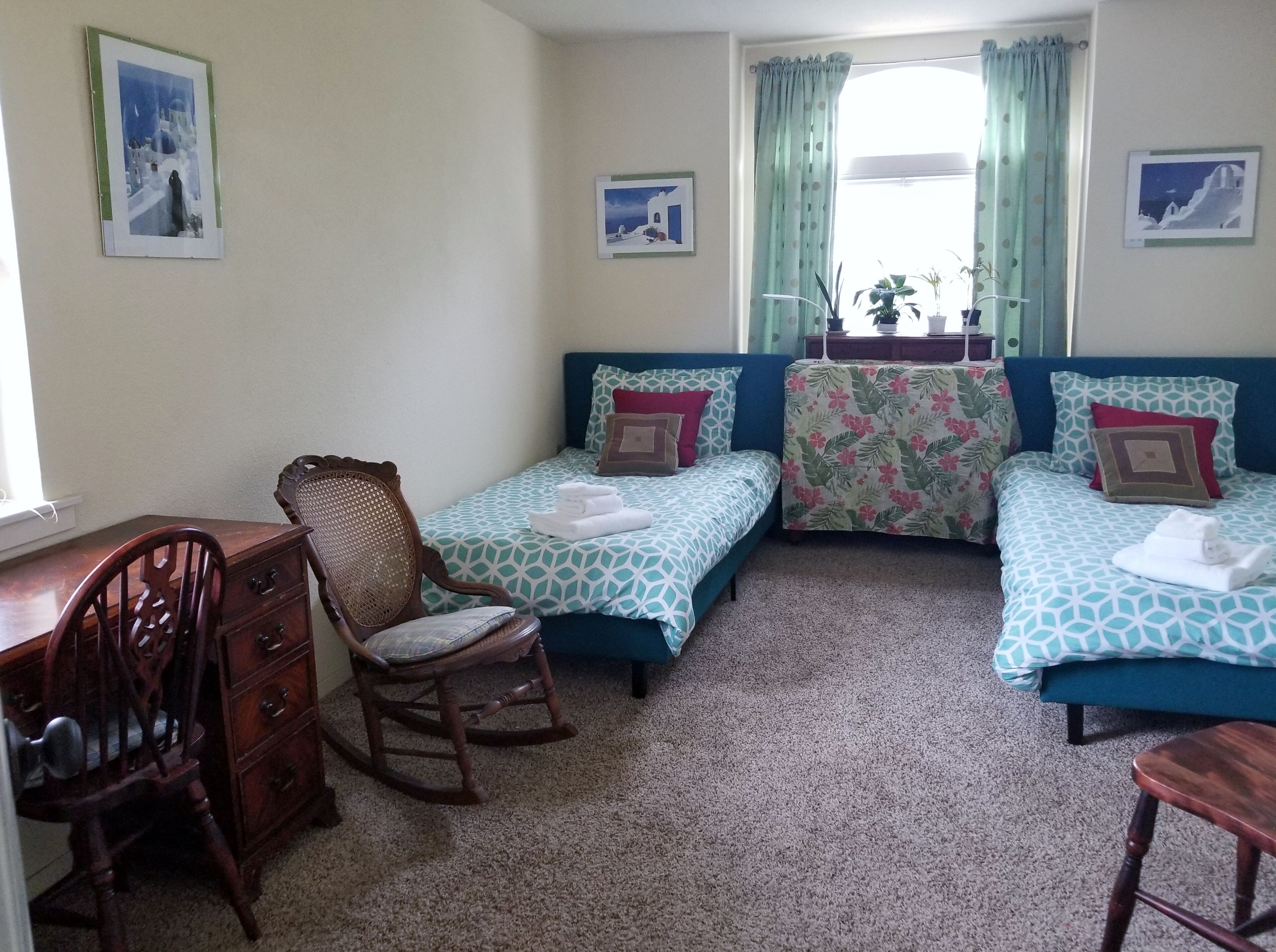 A room with two single beds, a wooden rocking chair, a desk, and a window with curtains.