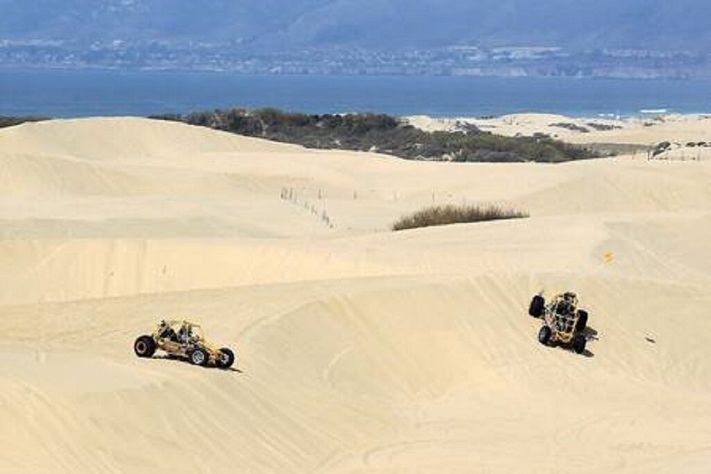 Wüstenlandschaft mit Sanddünen und zwei Geländefahrzeugen.