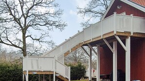 A covered outdoor area with a wooden deck and a red building.