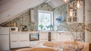 A kitchen with a sloped ceiling, white cabinets, a stove, and a window with plants.