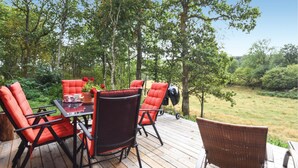 An outdoor deck with a table and chairs, surrounded by trees and a grassy area.