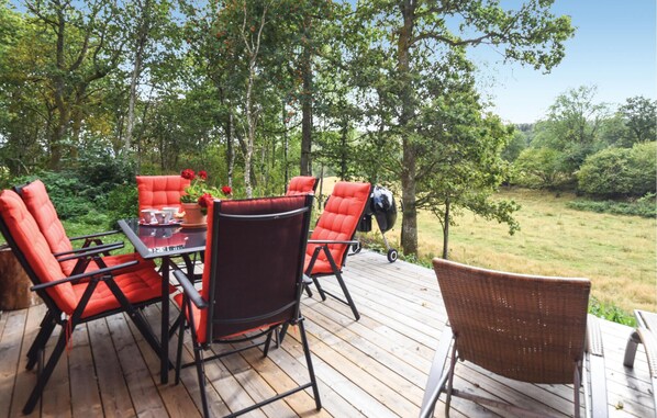 Una terraza al aire libre con una mesa y sillas, rodeada de árboles y césped.