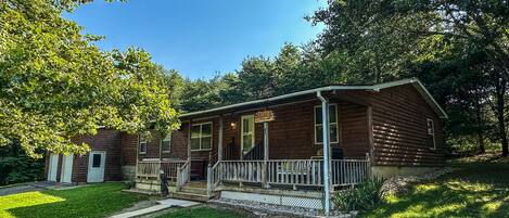 A log cabin with a porch, a front door, and a small front yard.
