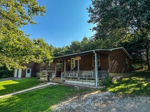 A log cabin with a porch, a front door, and a small front yard.