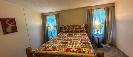 A bedroom with a wooden bed frame, a quilt with animal patterns, two bedside lamps, and a ceiling light.