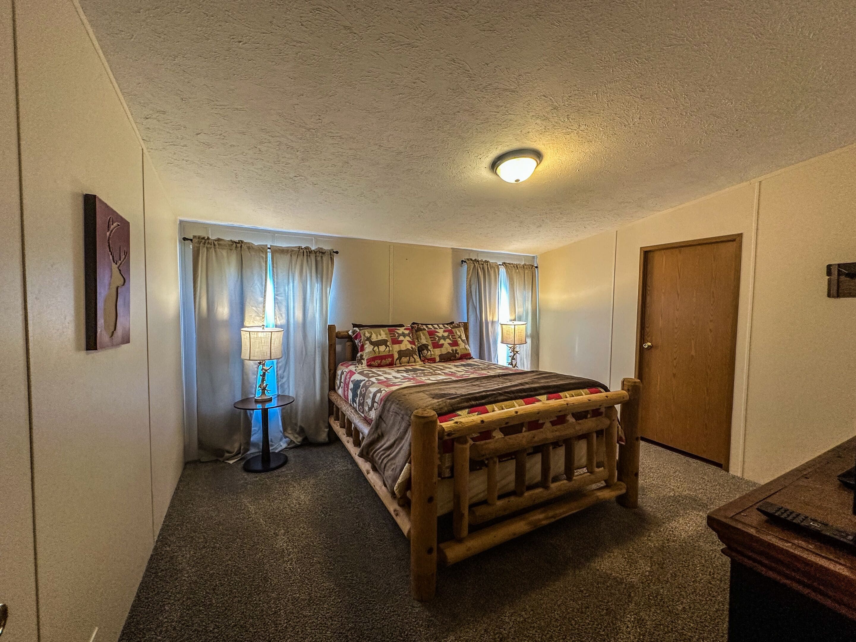 A bedroom with a wooden bed, two bedside lamps, a ceiling light, a door, and a wall-mounted picture.