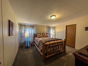 A bedroom with a wooden bed, two bedside lamps, a ceiling light, a door, and a wall-mounted picture.