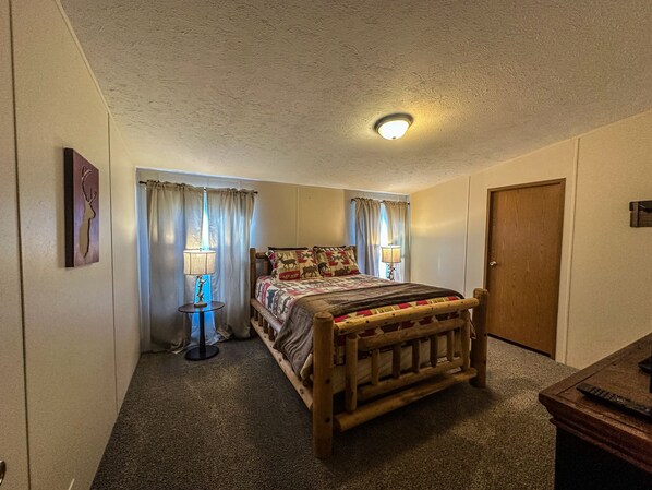A bedroom with a wooden bed, two bedside lamps, a ceiling light, a door, and a wall-mounted picture.