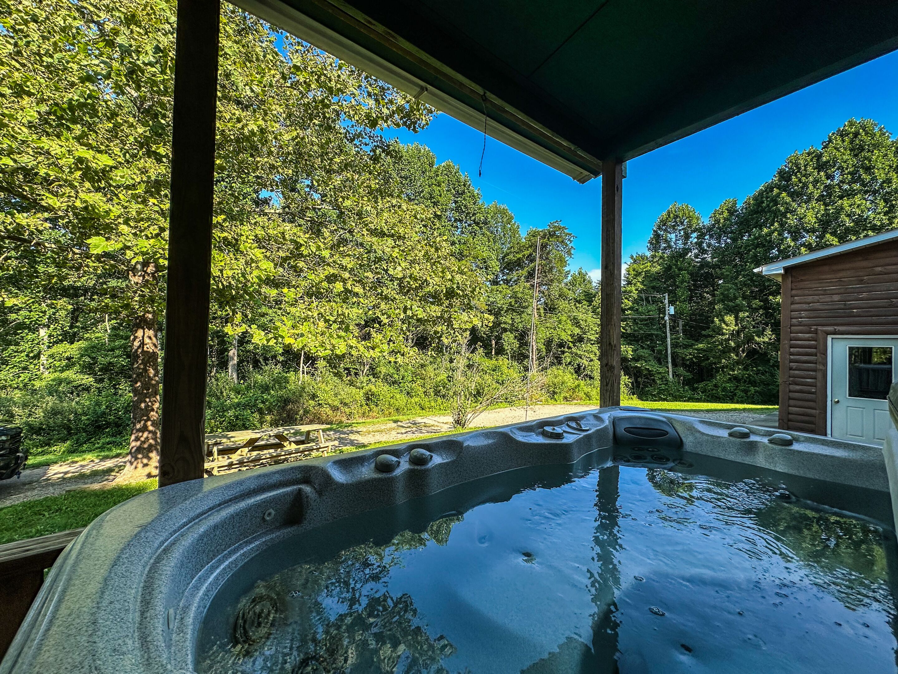 A hot tub under a covered area with a wooden cabin in the background.